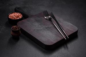 Wooden cutting board with kitchen appliances on a black concrete background photo