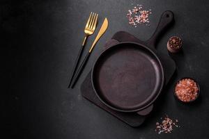 Brown iron empty pan with kitchen utensils on a dark concrete background photo