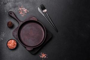 Brown iron empty pan with kitchen utensils on a dark concrete background photo