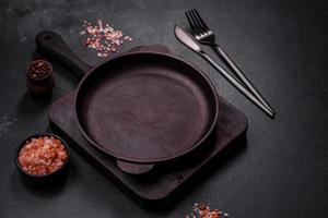 sartén vacía de hierro marrón con utensilios de cocina sobre un fondo de hormigón oscuro foto