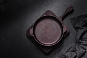 Brown iron empty pan with kitchen utensils on a dark concrete background photo
