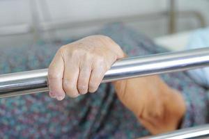 Asian elder senior woman patient holding bed rail while lie down with hope waiting her family in hospital. photo