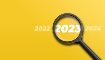 Magnifying glass magnifies the year 2023 between the years 2022 and 2024 on yellow background. Focusing on or analyzing the year 2023 for business planning concept. 3D illustration. photo