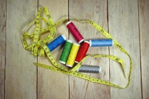 Spools of thread and basic sewing tools including pins, needle, a thimble, a tape measure and yarn scissors on a wooden table photo