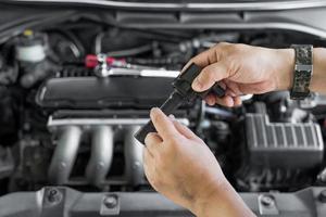 el técnico revisa la bobina de bujía vieja con marcas de quemadura en la bobina del motor en el servicio de mantenimiento del motor de gasolina en el garaje foto