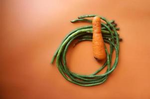 frijoles largos y zanahoria aislado sobre fondo naranja. foto