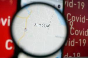 Surabaya, Indonesia on google maps under magnifying glass with Red Covid-19 text Background. photo