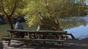 vecchio uomo seduta su panchina di il lago e guardare a il lago video