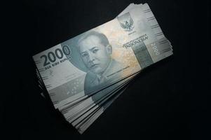 dinero en billetes de rupias indonesias, dos mil mil rupias, aislado en fondo negro, moneda indonesia. foto