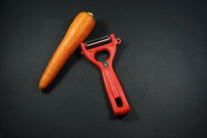 Raw peeled carrot with red peeler isloated on black, dark background. photo