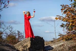 chica vestida de rojo sobre roca o estructura en ruinas de hormigón con serbal sobre fondo de otoño foto