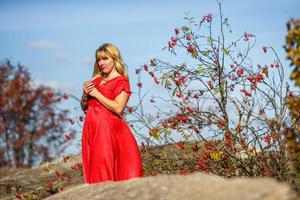 chica vestida de rojo sobre roca o estructura en ruinas de hormigón con serbal sobre fondo de otoño foto