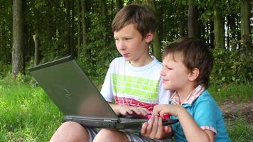 twee jongens zittend Aan de gras in de park en leren. een is Holding een tablet video