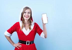 primer plano de una mujer feliz caucásica con ropa de santa apuntando al teléfono inteligente foto