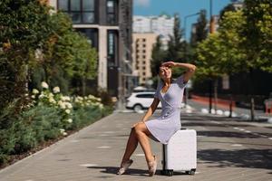 Pretty young woman sits on suitcase outside. photo