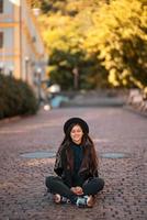 Young woman in hat sitting at city on cobblestone photo