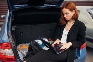 Woman working on laptop while sitting in trunk of car photo