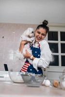 Smiling woman in kitchen holding cute white Maltese dog photo