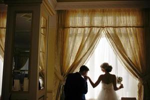 bride and groom standing in front of window photo