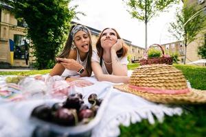 Two women having picnic together, laying on the park lawn photo