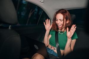 Beautiful woman is using laptop while sitting on back seat photo