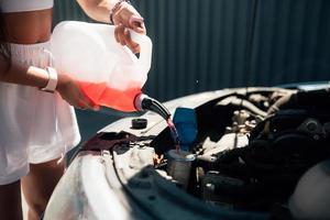 Young woman pouring antifreeze car screen wash liquid into car photo