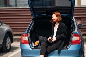 mujer que trabaja en la computadora portátil mientras está sentada en el baúl del auto foto