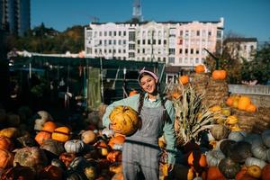 Happy farmer woman in a denim jumpsuit holds ripe pumpkin photo