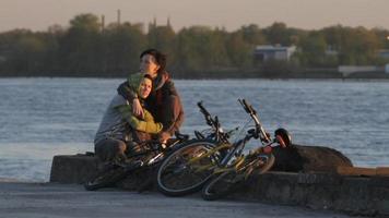 två kvinnor cyklister kramade tillsammans, på de riga frihamn längs de daugava flod, i riga, lettland. video