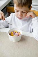 child eats colored cereals at the table, in a white kitchen. Boy's breakfast. Breakfast cereals before school. A quick snack of a schoolboy in the morning. photo