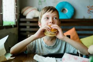 boy eating a big burger with a cutlet. Hamburger in the hands of a child. Delicious and satisfying chicken cutlet burger. Takeout food photo