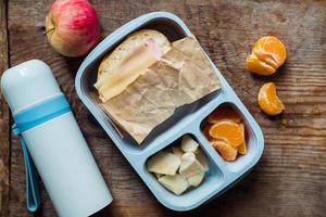 schoolboy lunch box with thermos on wooden background.apple,tangerine,sandwich in lunchbox and water bottle photo