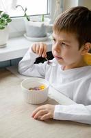 child eats colored cereals at the table, in a white kitchen. Boy's breakfast. Breakfast cereals before school. A quick snack of a schoolboy in the morning. photo