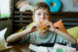 niño comiendo una hamburguesa grande con una chuleta. hamburguesa en manos de un niño. deliciosa y satisfactoria hamburguesa de chuleta de pollo. Sacar comida foto