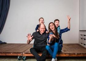Smiling family holding house shape while sitting on hardwood floor at home. Photoshoot of a family with 2 sons, white background. Warm family relationships. Young parents photo