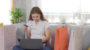 jeune femme faisant des achats en ligne à la maison. jeune femme avec des sacs à provisions près de ses achats avec carte de crédit. video