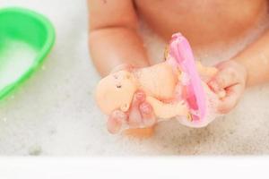 niña pequeña jugando con espuma en una bañera. chica se baña con una muñeca. niña jugando con juguetes en el baño foto