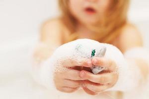 little baby girl with blond hair playing with foam in a bath tub. girl takes a bath. girl playing with toys in the bath photo