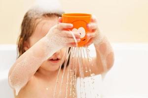 hijita de pelo rubio jugando con espuma en una bañera. la chica se baña. niña jugando con juguetes en el baño foto