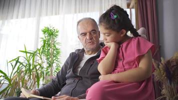grand-père et petit-fils lisant un livre. grand-père lit un livre à son petit-fils et le petit-fils écoute attentivement. video