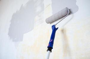 Roller on a wooden stick in gray paint is used to repaint the wall. Home renovation. photo