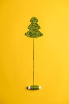 Knitted Christmas tree - a symbol of the New Year, with an unwound spool of thread like a trunk, on a yellow background. Top view. photo