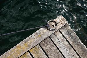 viejo muelle de madera envejecido con un anillo de amarre de metal y una cuerda estirada, contra el telón de fondo de un mar con olas. copie el espacio vista superior. foto