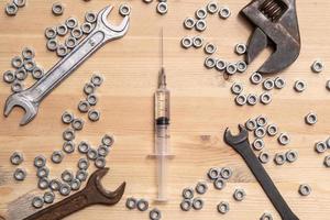 Syringe with a medicine lies on a wooden table among a variety of wrenches and metal nuts. Vaccine production concept. Top view. photo