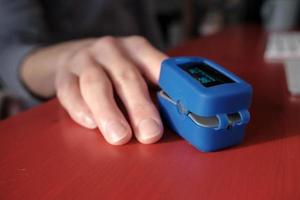 Woman uses a pulse oximeter to measure pulse rate and blood oxygen levels on a red table in an apartment.