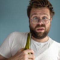 Unshaven man with tousled hair suffers from a hangover, he hugs an empty wine bottle, makes a strange grimace and looks unkempt. photo