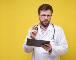 Focused doctor contemplating a diagnosis, holding a tablet and a stylus. Copy Space. Yellow background. photo