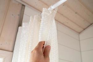 Hand closes a waterproof curtain in the bathroom, which covers the shower and prevents moisture from entering the floor. Bottom view. photo