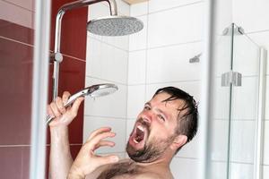 hombre europeo cantando en voz alta en la ducha usando una lata de agua como micrófono. foto