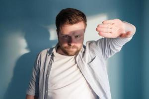 Serious man stops sunlight with hand and creates a shadow on his face. photo